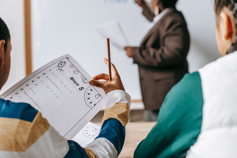 Students in a classroom focus on worksheets while the teacher conducts a lesson